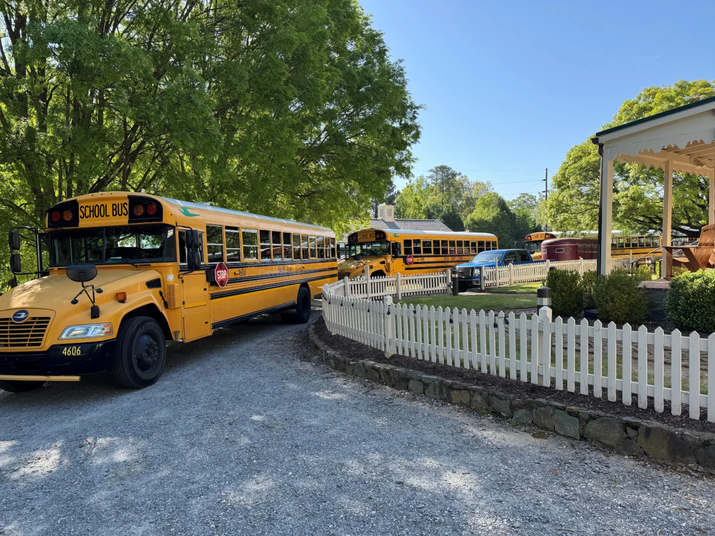 two school busses in driveway along a white picket fence
